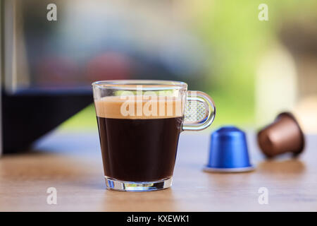 Tasse Kaffee und Espresso Kapseln auf Holztisch, unscharfen Hintergrund, Detailansicht mit Details Stockfoto
