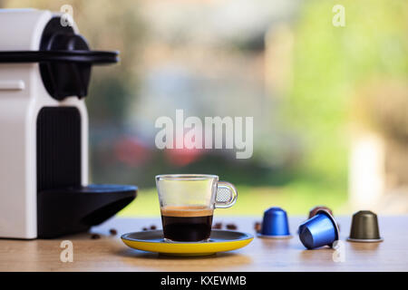 Tasse Kaffee und Espresso Maschine und Kapseln auf Holztisch, unscharfen Hintergrund, Detailansicht mit Details Stockfoto