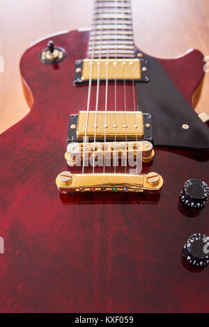 Glänzend Weinrot Gitarre mit goldene Hardware auf einem Holztisch mit Fokus auf den Stop Bar Stockfoto