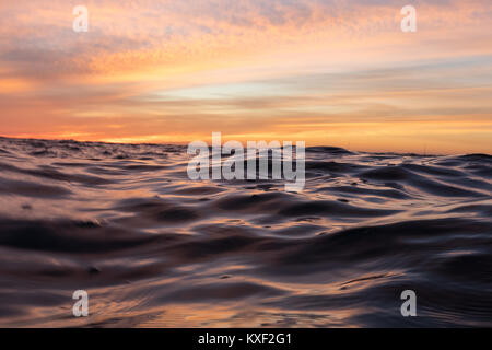 Wellen erstrecken sich über die Oberfläche des Ozeans während einer lebendigen Sonnenuntergang Nachleuchten in Los Angeles, Kalifornien. Stockfoto