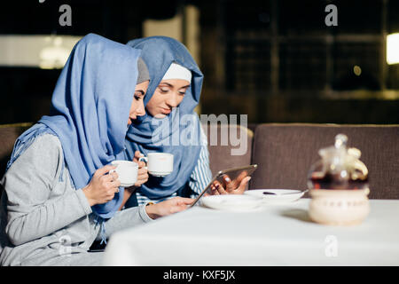 Ziemlich muslimische Frau mit Tablette im Cafe Stockfoto