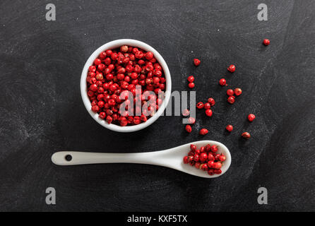 Roter Pfeffer Gewürz Samen in Porzellan Schüssel und Löffel, schwarzer Hintergrund Stockfoto