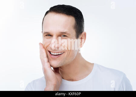 Positive freudige Mann seine Wange berühren Stockfoto