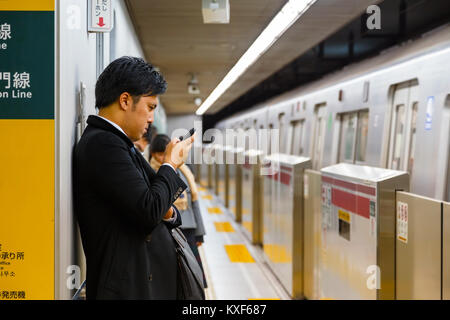 TOKYO, Japan - 28. NOVEMBER 2015: Unbekannter japanischen U-Bahn Pendler nutzt sein Gerät, während sie wartet auf einen Zug auf einer Plattform Stockfoto