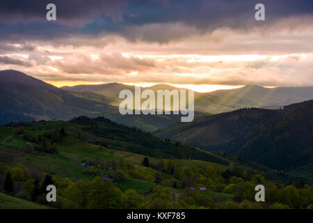 Wunderschöne bergige Landschaft bei Sonnenuntergang. Lichtstrahlen brechen durch schwere Wolken. Rolling Hills mit ländlichen Felder im Schatten. Spektakuläre autolöscher Stockfoto