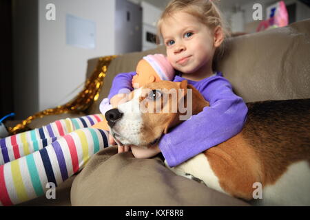 Mädchen umarmt sie beagle Hund. Kleines Mädchen mit ihrem Hund auf der Couch. Mädchen und pet die besten Freunde. Stockfoto