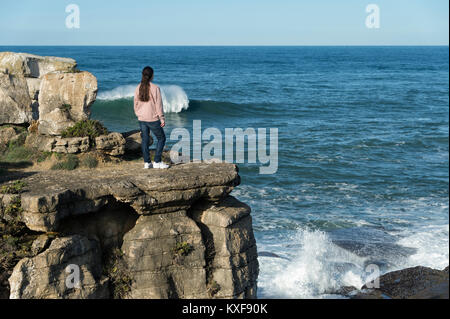 Frau stehen am Rand von einem Felsvorsprung auf die Wellen schauen. Stockfoto