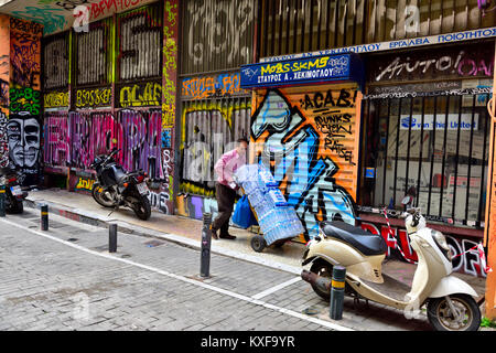 Mann wheeling Wasserflaschen an Hand Warenkorb vor bunten Graffiti in der Innenstadt von Athen, Griechenland Stockfoto