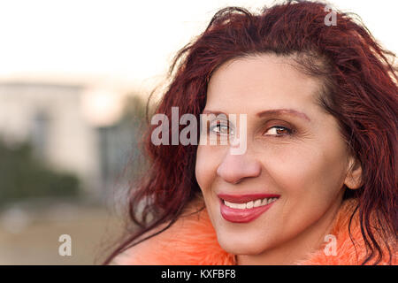 Nahaufnahme von einem schönen Lächeln, reife Frau mit leichtem strabismus der Venus trägt orange Pelz Kragen Stockfoto