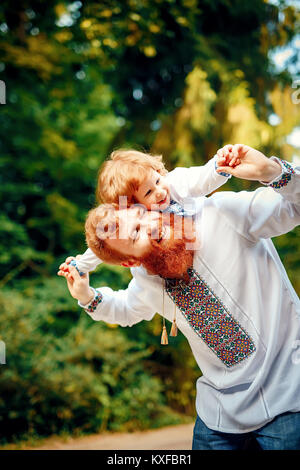 Rot - Heared Vater und rot-Heared Sohn Spaß haben in einem Park in einer traditionellen weißen Hemden mit Ornament Stockfoto