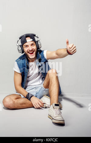 Im Rhythmus der Musik. Entspannt junger bärtiger Mann im Kopfhörer in der Nähe der graue Wand Sitzen und Hören der Musik. Stockfoto