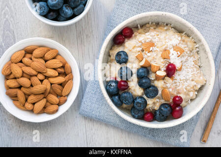 Haferflocken porridge Bowl mit Heidelbeeren, Preiselbeeren, Mandeln und kokosflocken auf grauem Hintergrund. Ansicht von oben, Nahaufnahme Stockfoto