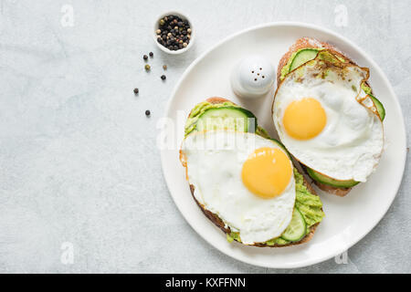 Gesundes Frühstück Toast mit Spiegelei, Avocado und Gurke auf weiße Platte. Ansicht von oben und kopieren Sie Platz für Text. Konzept der gesunden Ernährung, gesunde lif Stockfoto