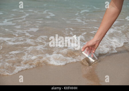 Hand hält eine Flasche mit einem Brief, der nach innen durch das Meer eingefügt. Stockfoto