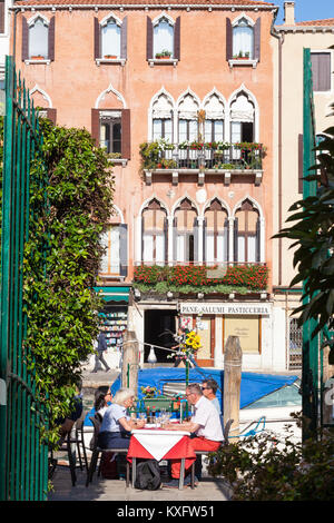 Touristen Speisen im Open Air Restaurant Tabellen in Cannaregio, Venice, Italien neben den Cannaregio-kanal durch Grün im öffentlichen Park gesehen Stockfoto