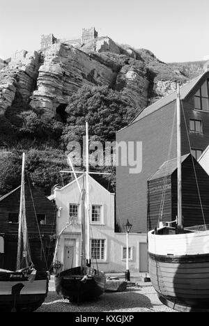 Net Hütten und Boote am Strand von Hastings, East Sussex, mit dem östlichen Hügel im Hintergrund Stockfoto