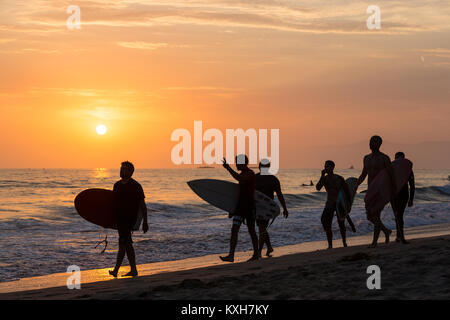 Eine Gruppe junger Surfer Spaziergänge über den Sand bei Sonnenuntergang in Los Angeles, Kalifornien. Stockfoto