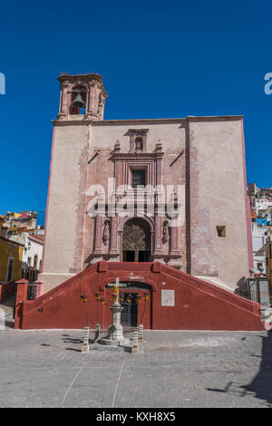 Vordere Aufnahme eines alten Steinkirche, mit einem Glockenturm und einem roten doppelseitige Treppe, in der Plaza San Roque, mit klaren blauen Himmel, in Guanajuato Stockfoto