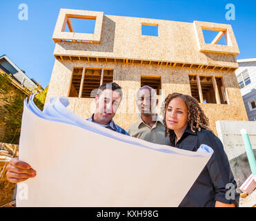 Ein paar Bewertungen Pläne für ein Haus mit ihrem Auftragnehmer/Architekt auf der Baustelle. Stockfoto