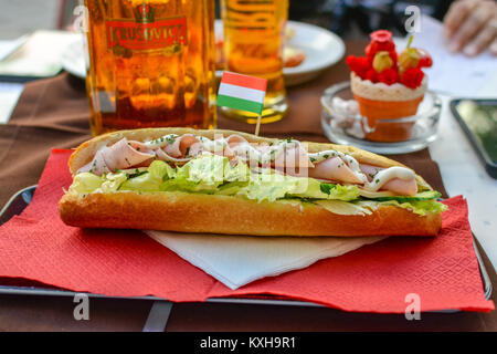 Ein Club Sandwich mit Truthahn, Schinken, Salat und Mayo auf einem Baguette, und zwei Biere an ein Café im Freien in Budapest, Ungarn, die ungarische Flagge Stockfoto