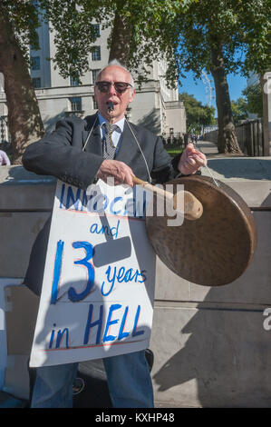 Ein Mann mit einem Plakat "Unschuldigen und 13 Jahre in der Hölle" knallt einem Gong zu feiern, Shaker Aamer ist befreit werden. Die Aktivisten, die die regelmäßige wöchentliche Mahnwachen noch gehalten haben Sorgen, er kann festgehalten werden, um ihn zu stoppen, die Beweise für Folter. Stockfoto