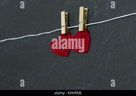 Rote Herzen hängen in einem Winkel von Clothespin vor der Tafel Hintergrund Stockfoto