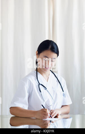 Lächelnde Ärztin, die in der Klinik ein Rezept am Tisch schreibt Stockfoto