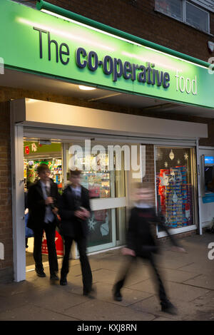 Großbritannien, England, Bramhall, Stockport, Cheshire, Dairyground Road, Co-op-Food Store Eingang bei Dämmerung, Schüler auf dem Weg nach Hause im Winter Stockfoto