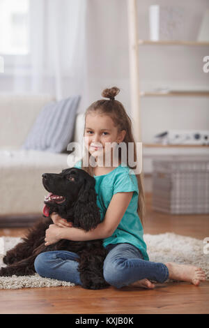 Portrait von niedlichen Mädchen umarmen Hund, während auf dem Teppich zu Hause sitzen Stockfoto