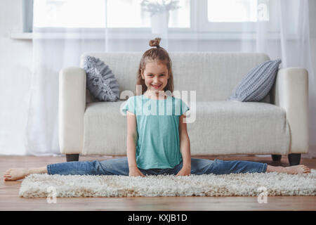 In voller Länge Porträt von lächelnden Mädchen tut Splits auf dem Teppich im Wohnzimmer zu Hause Stockfoto