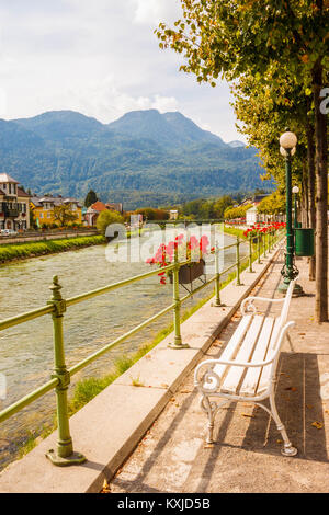 Freie weisse Sitzbank am Riverside Promenade mit Blick auf den Fluss Traun und die Berge an einem sonnigen Sommertag in einem Kurort Bad Ischl, Österreich. Stockfoto