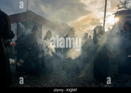 Antigua, Guatemala - 19. April 2014: Silhouette der Männer in schwarzen Roben und Hauben Räucherwerk verbreiten sich in einer Strasse der Stadt Antigua während einer pro Stockfoto