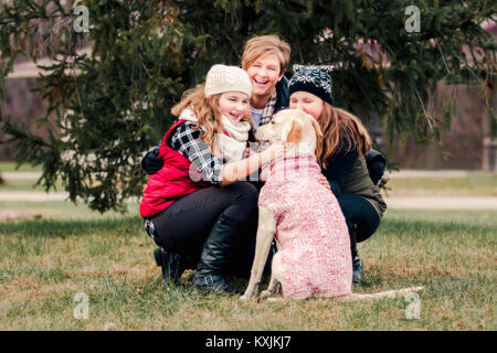 Schwestern und ihre Mutter ducken zu Hund im Garten Stockfoto