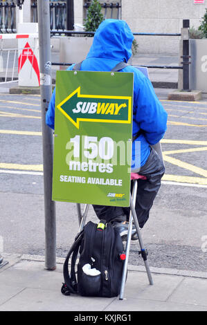 Eine Person sitzt auf einem klapphocker oder Sitz tragen ein Sandwich board Werbung in einem Fast Food Restaurant oder Imbiss zur Verfügung. lustige Wange Stockfoto