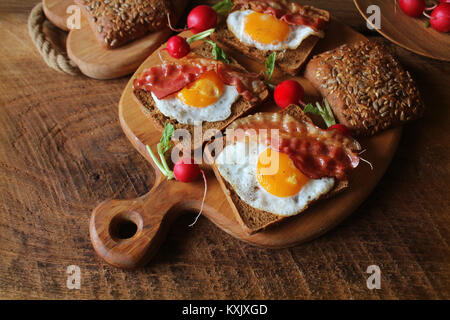 Frühstück mit knusprigem Speck, Spiegelei und Brot. Sandwiches auf Schneidebrett. Rustikale Tabelle Stockfoto