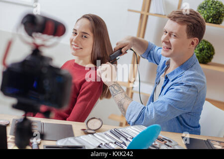 Emotionale Mann drücken die Haare von seinem Assistenten mit seinem lockenstab Stockfoto