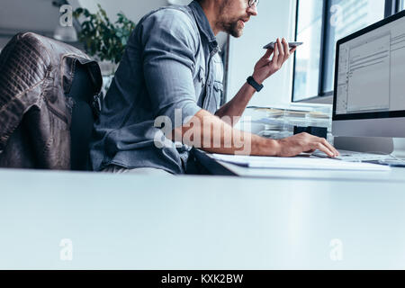 Geschäftsmann mit Mobiltelefon im Büro und Arbeiten am Computer. Junge Unternehmer Gespräch am Handy und Computer im Büro. Stockfoto