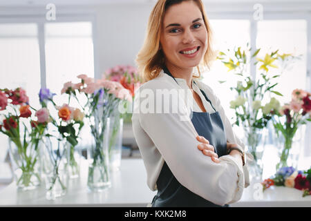 Portrait von glücklich und zuversichtlich florist Eigentümer in Ihrem eigenen Blumenladen. Kaukasische Frauen tragen Schürze mit ihren Armen an ihrer Flower Shop gekreuzt. Stockfoto