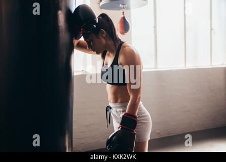Weibliche Boxer eine Pause von ihrer Praxis. Frau Boxer nach vorne auf einem riesigen Boxsack ein Boxing Studio zu ruhen. Stockfoto