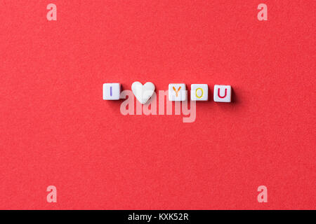 Satz ich liebe Dich aus Buchstaben, Würfel und einzelne Herzen Form weißer Kandiszucker Streuen auf dunklen roten Hintergrund. Romantik Valentinstag Muttertag Stockfoto