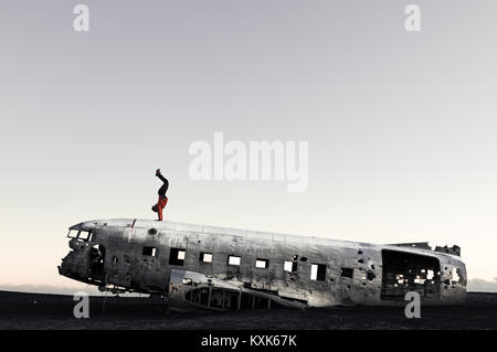 Handstand auf einem abgestürzten Flugzeug in Island während des Sonnenuntergangs. Abenteuer und Leben ein bisschen gefährlich. Erstellen eines neuen Classic Foto bei einer Sehenswürdigkeit. Stockfoto