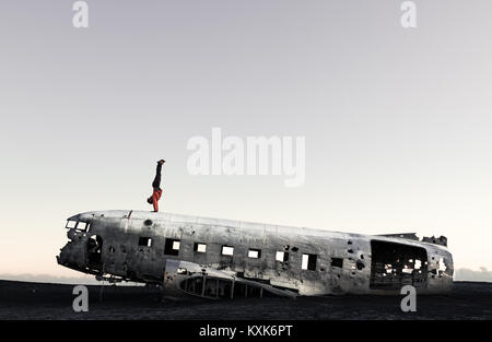 Handstand auf einem abgestürzten Flugzeug in Island. Sólheimasandur. Schwarzer Sand und ein Wrack. Wahrzeichen. Stockfoto