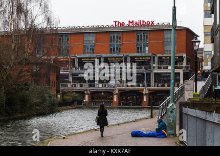 Eine Frau übergibt einen Obdachlosen Mann auf der Seite des Kanals, wie sie Spaziergänge in Richtung der Mailbox Einkaufszentrum in Birmingham. Stockfoto