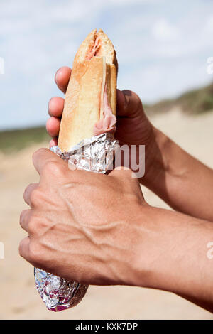 Nahaufnahme eines jungen kaukasischen Mann essen einen Schinken und Käse Sandwich, in Alufolie, im Freien Stockfoto