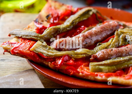 Nahaufnahme eines Segments der Coca de Recapte, ein typisch katalanischen herzhaften Kuchen ähnlich wie Pizza, mit gegrillten Auberginen und rotem Pfeffer und Fleischwurst, getroffen Stockfoto