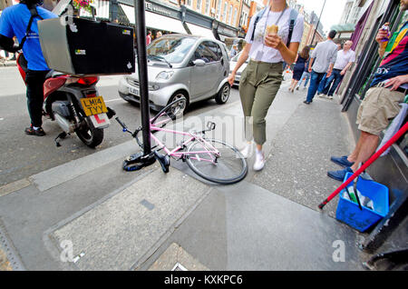 London, England, UK. Fahrrad angekettet an einen Pfosten und Sperrung der Bordstein - stolpergefahr Stockfoto