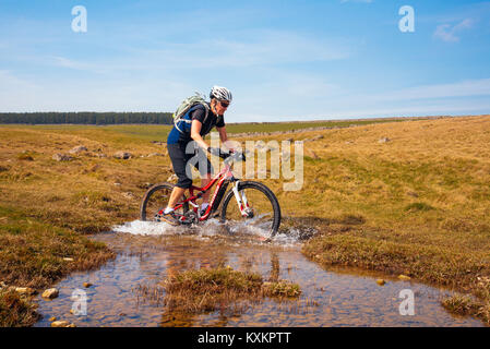 Weibliche Mountainbiker Spritzwasser durch eine Furt auf Crosby Ravensworth fiel in den Yorkshire Dales National Park Stockfoto