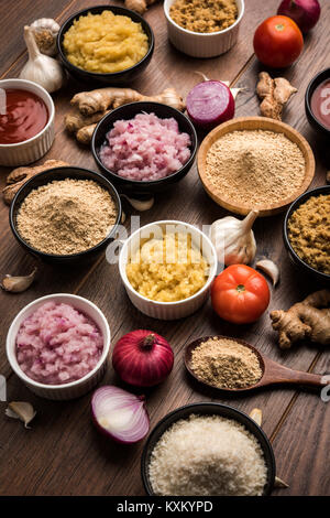 Ingwer, Knoblauch, Zwiebel und Tomatenmark und Pulver in und rohen Form. Gruppe von grundlegenden indischen Lebensmittelzutaten über Holz- Hintergrund. Selektiver Fokus Stockfoto