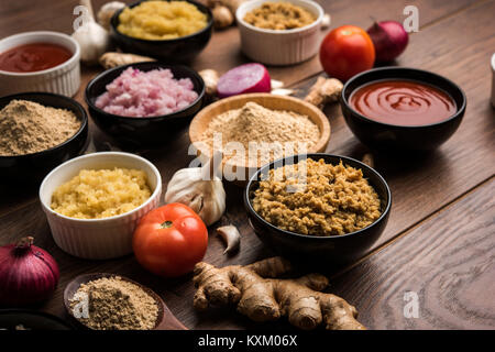 Ingwer, Knoblauch, Zwiebel und Tomatenmark und Pulver in und rohen Form. Gruppe von grundlegenden indischen Lebensmittelzutaten über Holz- Hintergrund. Selektiver Fokus Stockfoto