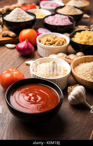 Ingwer, Knoblauch, Zwiebel und Tomatenmark und Pulver in und rohen Form. Gruppe von grundlegenden indischen Lebensmittelzutaten über Holz- Hintergrund. Selektiver Fokus Stockfoto